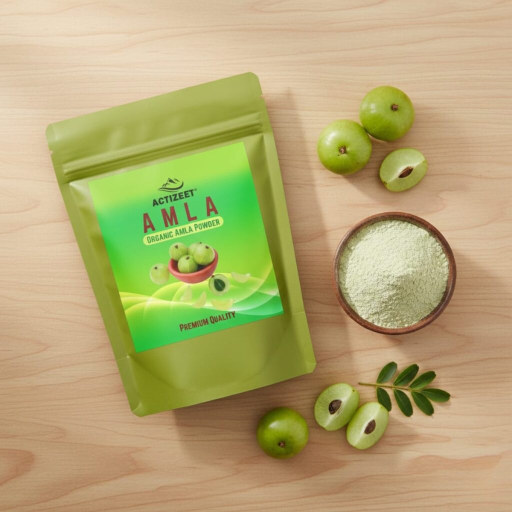 Overhead shot of Amla powder, sliced fruit, and green leaves on an oak wood surface.