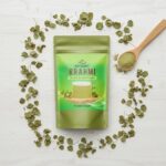 Top-down flat lay of Brahmi powder pouch with dried leaves and a wooden spoon.