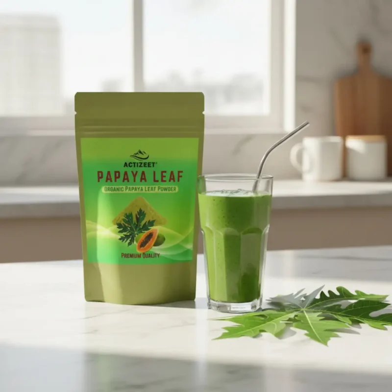 A healthy green smoothie in a glass next to ACTIZEET Papaya Leaf Powder on a marble countertop